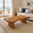 Live edge coffee table with sculpted slab top and broad solid wood legs in a coastal room