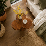 Modern end table with sculpted pedestal form and warm finish beside layered bedding