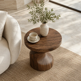 Modern end table with an artistic base and warm dark finish beside soft lounge seating