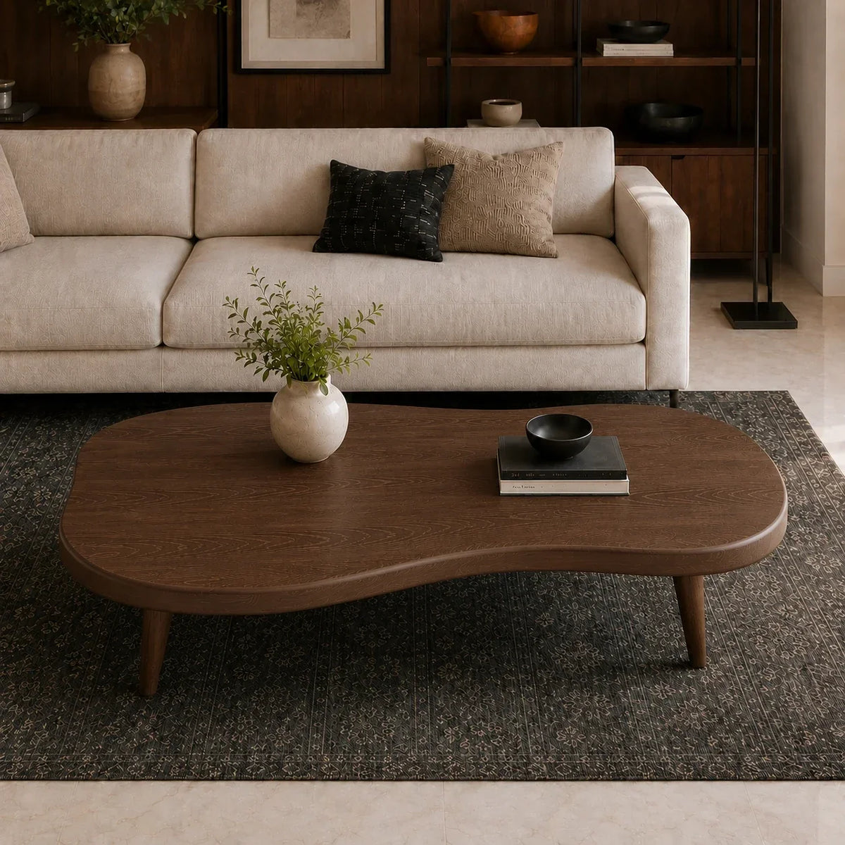 A modern wavy wooden coffee table in a warm medium brown finish, styled in a living room setting on a dark textured rug in front of a cream-colored sofa.