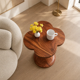 Modern end table with artistic pedestal form and warm finish beside lounge seating