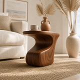 Modern end table with artistic base and warm finish beside lounge seating indoors