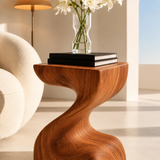 Designer side table with sculpted lines and visible grain in a calm living room interior