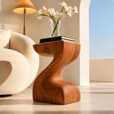 Modern end table with an artistic pedestal form and warm finish beside lounge seating