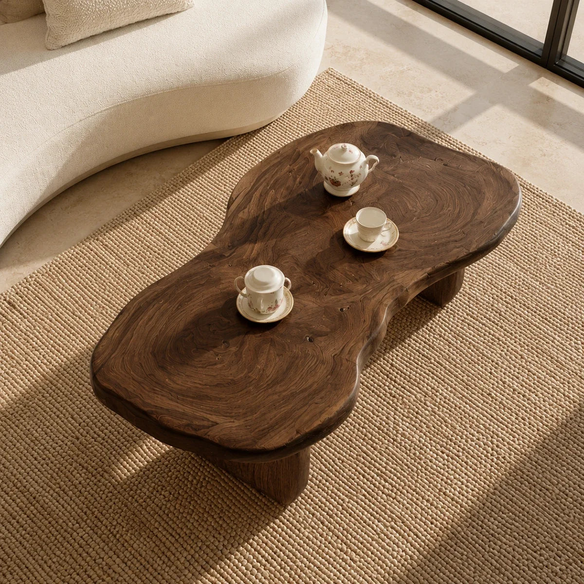 Modern coffee table with freeform top and dark wood tone beside curved lounge seating