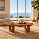 Living room coffee table with sculpted supports and warm finish in a sunlit home