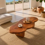 Modern coffee table with freeform top and warm wood tone beside soft lounge seating
