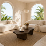 Organic modern coffee table styled between curved sofas in a calm coastal interior