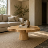 This pedestal coffee table features a broad round top and smooth handcrafted finish