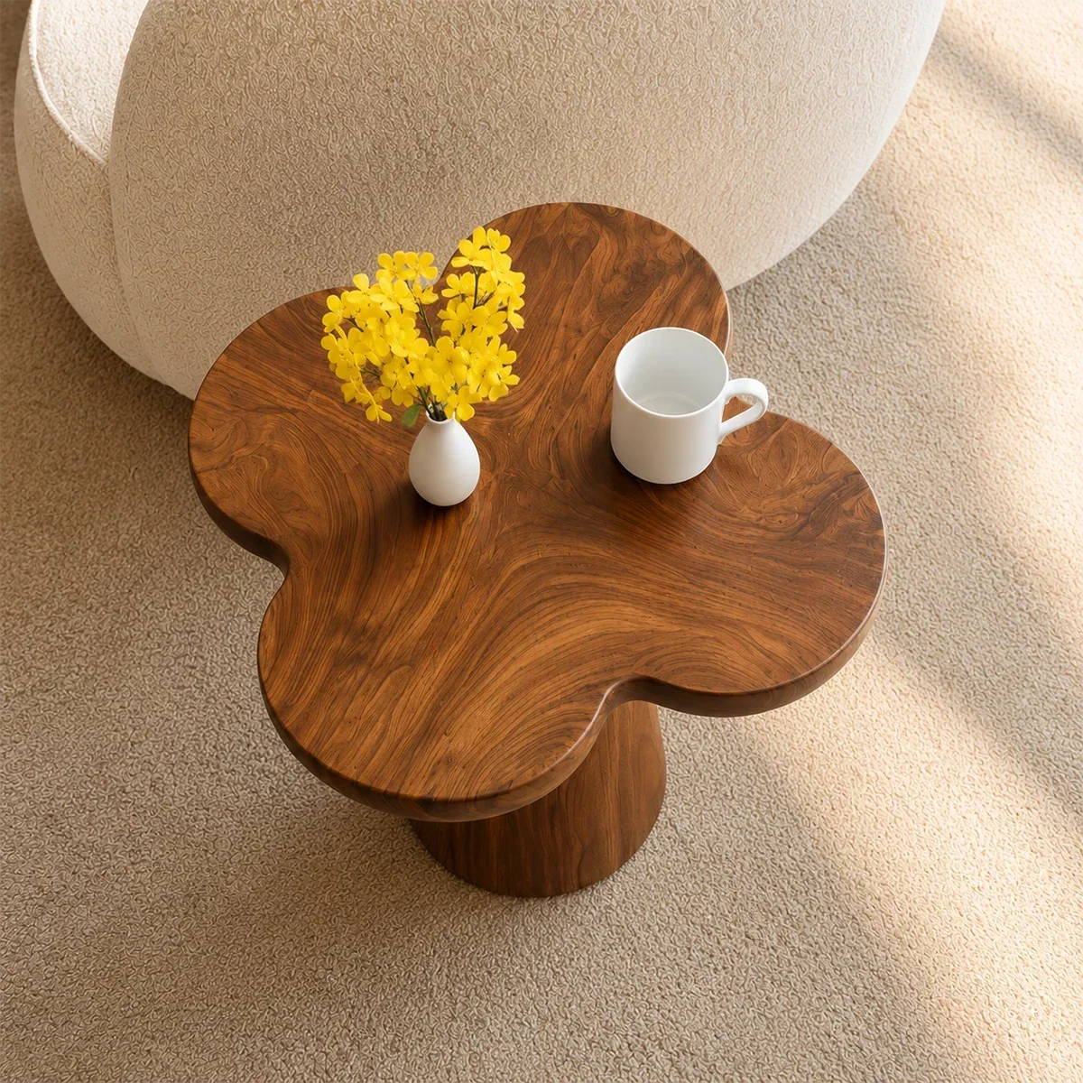Modern end table with artistic pedestal form and warm finish beside lounge seating