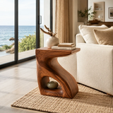 Sculptural end table with open shelf and warm wood tone finish beside coastal seating