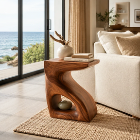 Sculptural end table with open shelf and warm wood tone finish beside coastal seating