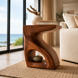 Modern end table with an open base and warm finish beside a soft lounge chair indoors