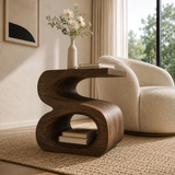 Modern end table with artistic open form and warm finish beside a rounded lounge chair