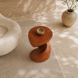 Modern end table with an artistic pedestal form and warm finish beside lounge seating