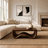 Living room coffee table with a broad top and wave inspired base beside neutral seating
